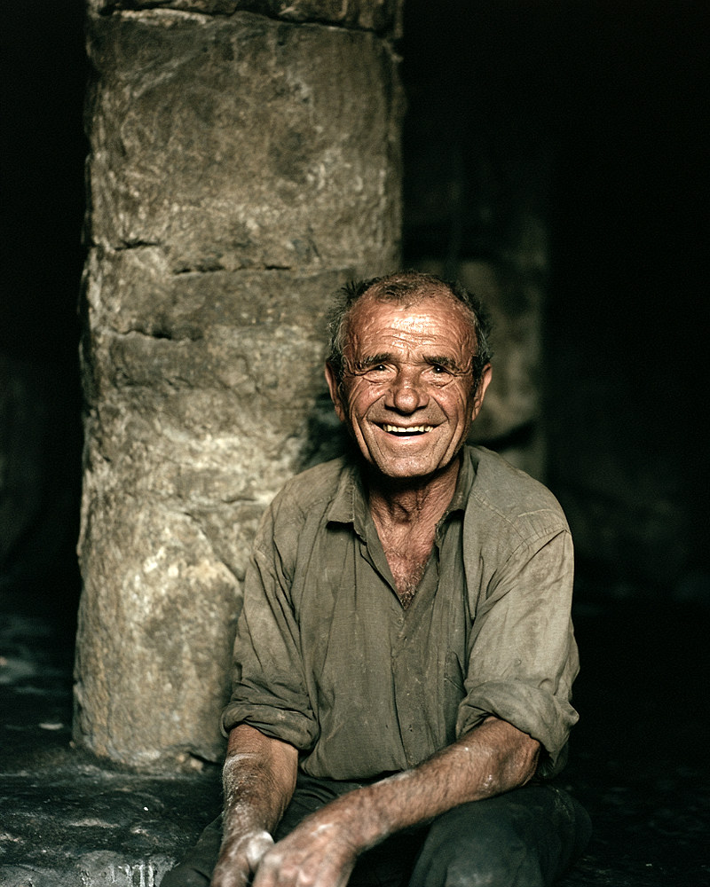 Frank Whitlow, an old man smiling warmly in a dim, torch-lit stone cave