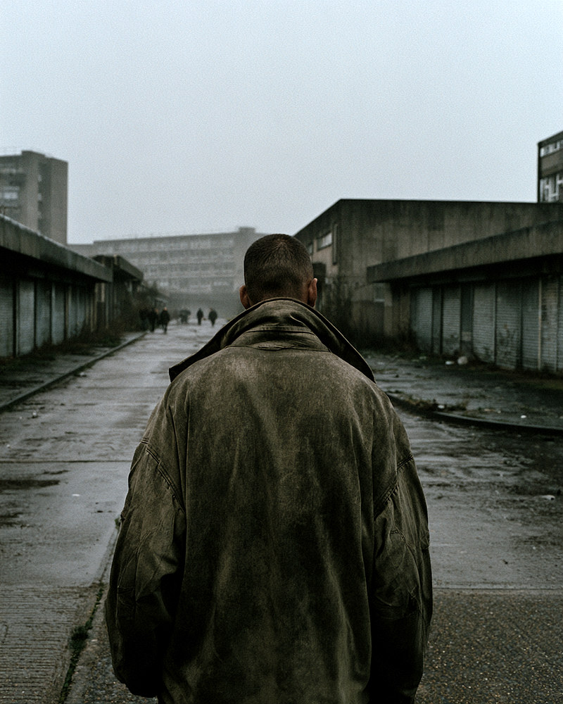 Vernon, seen from behind, walking away down a wet grey estate street